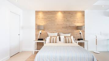 Ein modernes Schlafzimmer mit einem Holz-Kopfteil, einem großen Bett mit gestreifter Bettwäsche, zwei Nachttischen mit Lampen und einem weißen Kleiderschrank.