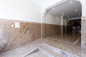 Un couloir au sol en marbre, bordé de carreaux, et un escalier menant à un niveau supérieur.