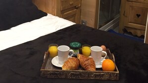 A wooden cabin interior with a bed, a tray with croissants, orange, and beverages. - Studio - VAL THORENS (Les Belleville)