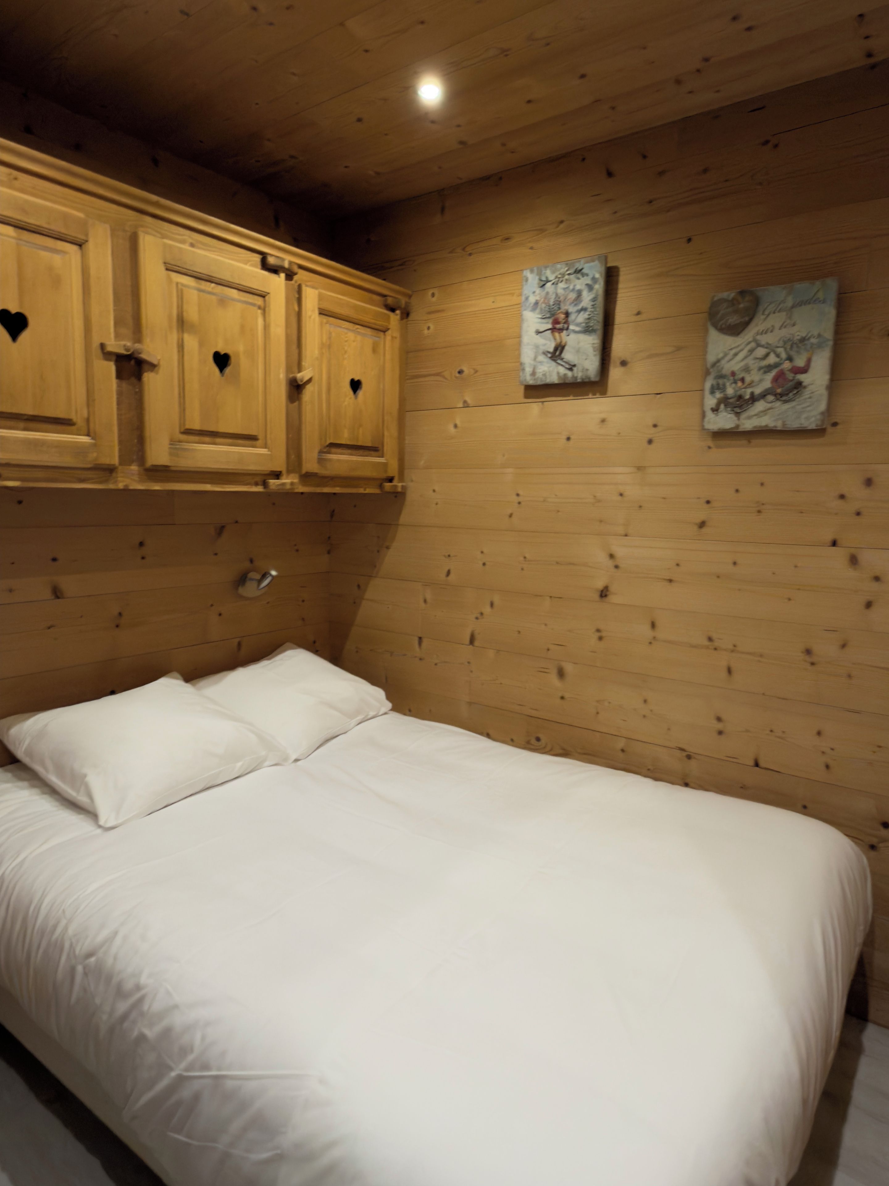 A bedroom with a wooden headboard, a bed with white bedding, and two paintings on the wall.