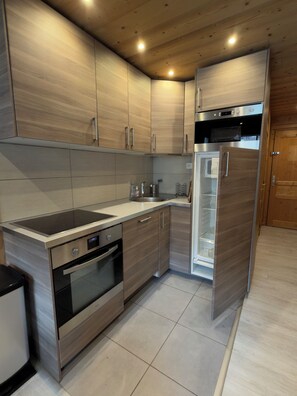 A modern kitchen with stainless steel appliances, wooden cabinetry, and a built-in dishwasher. - Studio - VAL THORENS (Les Belleville)