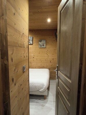 A wooden-paneled room with a bed, two wall-mounted artworks, and a door. - Studio - VAL THORENS (Les Belleville)