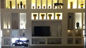 A modern living room with a flat-screen TV, shelves with decorative items, and a seating area with a sofa and coffee table. - 200m from the beach, magnificent architect's apartment with rooftop and sea view (Hammamet)