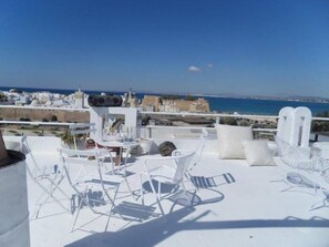 Eine Dachterrasse mit weißer Möbel und Blick auf das Meer und die Stadt.
