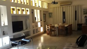 A modern living room with a sofa, a glass coffee table, a TV, and a dining area with a table and chairs. - 200m from the beach, magnificent architect's apartment with rooftop and sea view (Hammamet)