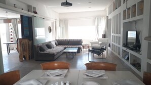 A modern living room with a sectional sofa, a dining table set with plates, and a television on a stand. - 200m from the beach, magnificent architect's apartment with rooftop and sea view (Hammamet)