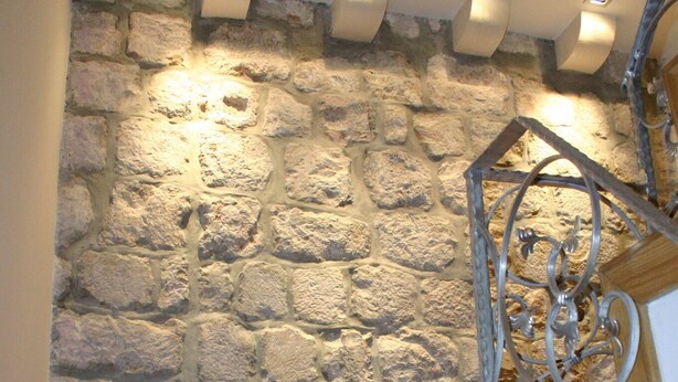 Una escalera con pared de piedra de fondo, escalones de madera y barandilla de metal.