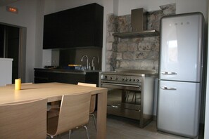Une cuisine moderne avec une table en bois, des chaises, un four en acier inoxydable, un réfrigérateur à deux portes et un pare-feu en pierre.