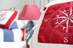 A close-up of a red and white pillow with a compass design, part of a bed with a white and blue striped pillow.