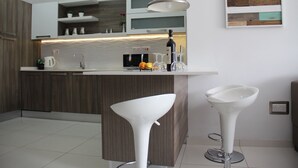 Una cucina moderna con un piano di lavoro bianco, mobili in legno e due sgabelli da bar bianchi.