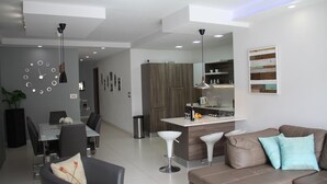 Un soggiorno moderno con un divano in pelle marrone, un'area pranzo con tavolo in vetro e una cucina con piano di lavoro bianco.