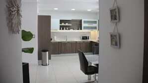 Una cucina moderna con mobili bianchi, un forno a microonde e un lavello. C'è un'area pranzo con una sedia nera e un tavolo.