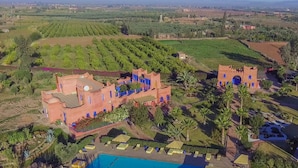 Una extensa propiedad con varias construcciones, incluyendo una estructura tipo castillo con puertas azules, rodeada de exuberantes jardines y palmeras.