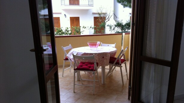 Une terrasse ouverte avec une table ronde et des chaises, une porte vitrée donnant sur l’extérieur et une vue sur un immeuble doté de balcons.