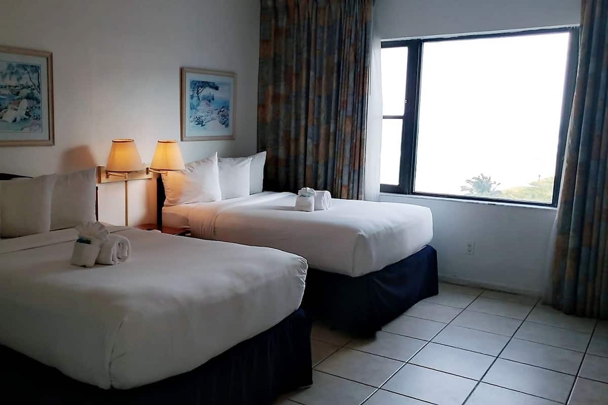 Ein Hotelzimmer mit zwei Betten, einem großen Fenster mit Vorhängen und zwei Wandlampen.