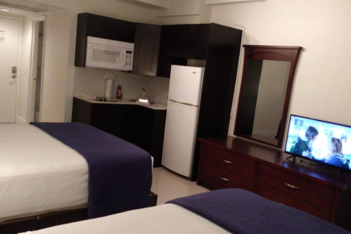 Ein Hotelzimmer mit zwei Betten, einer Mikrowelle, einem Kühlschrank, einem Fernseher und einer kleinen Küchenzeile.