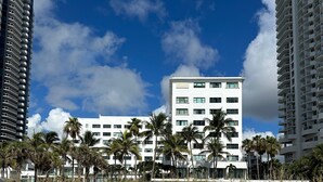Hotel sulla spiaggia con diversi piani, palme e cielo sereno.