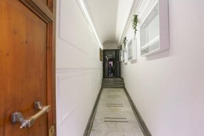 A hallway with a wooden door on the left, white walls, and a marble floor.