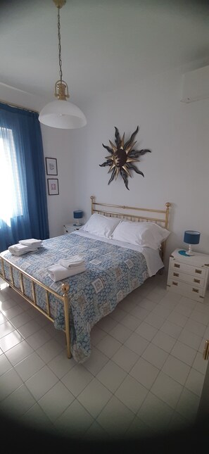 Un lit bien fait, avec une couvre-lit à motifs et des oreillers, une table de chevet avec une lampe et un soleil décoratif accroché au mur.