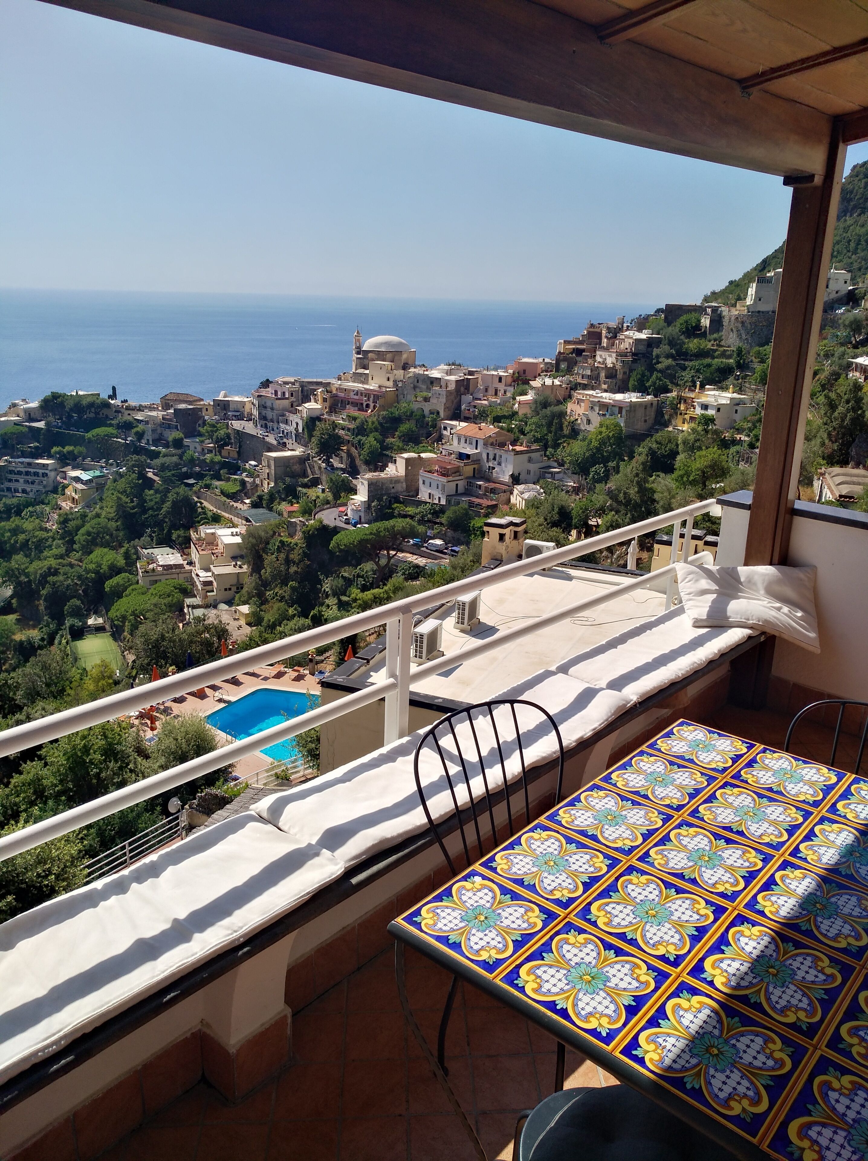 Ein Balkon mit Blick auf eine Küstenstadt, einen Pool und einen gefliesten Tisch.