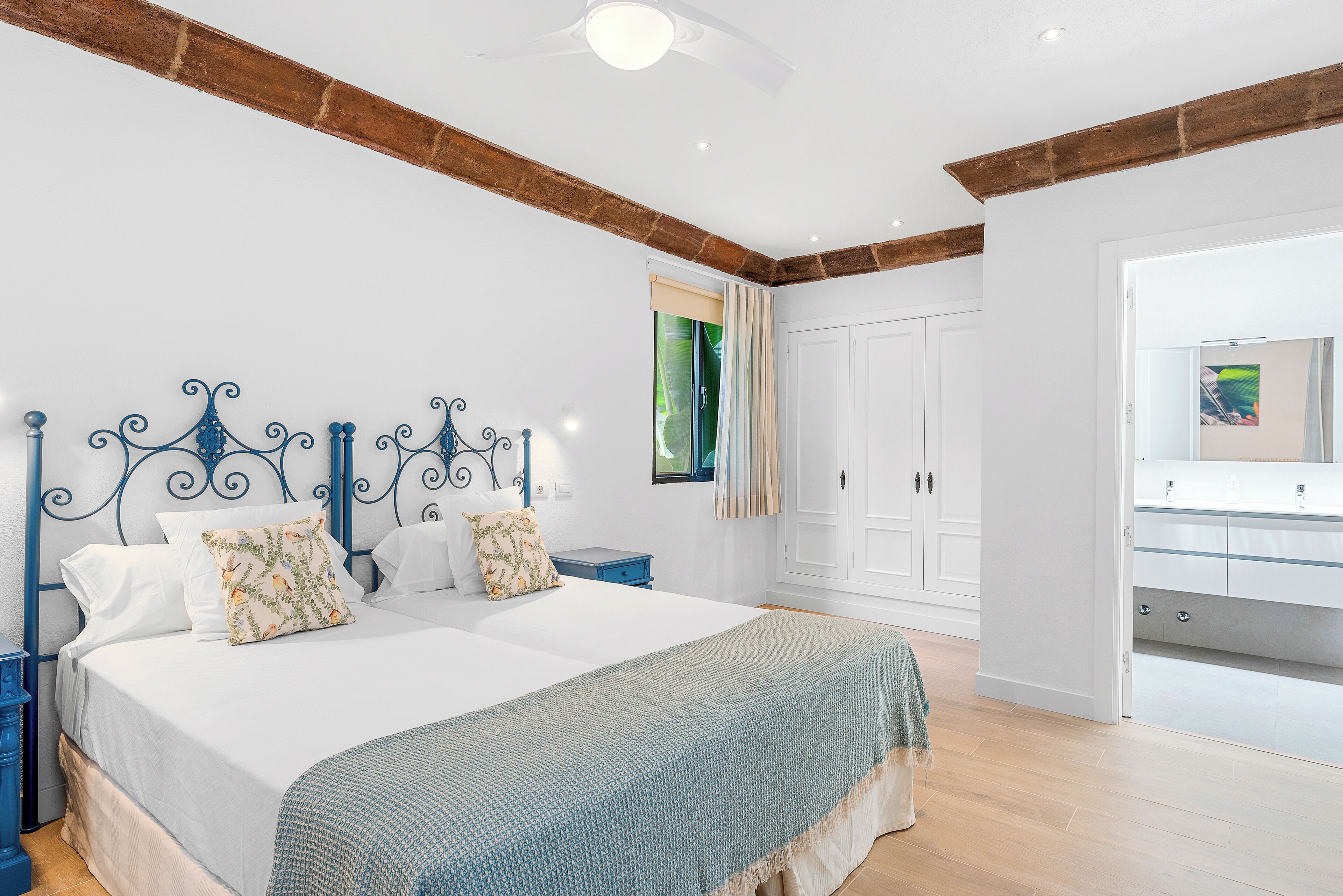 A bedroom with a large bed, a wooden ceiling beam, a white wardrobe, and a bathroom with a mirror.