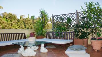 A patio with a glass table, two cushioned benches, and a small white statue.