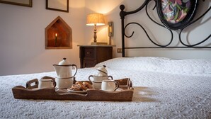A neatly arranged breakfast tray with tea pots, cups, and cookies on a bed with a lace cover.