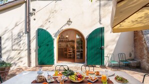 An outdoor dining area with a table set for breakfast, featuring a variety of fruits, pastries, and beverages.