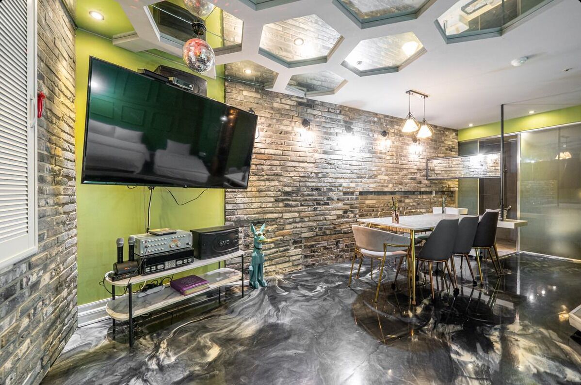 A modern living room with a flat-screen TV, a stone wall, a dining area with chairs, and a marble floor.