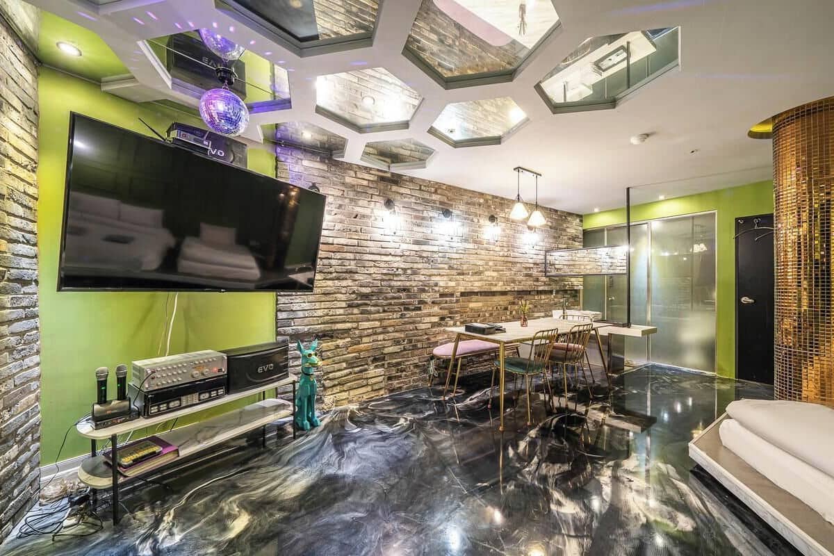 Una sala de estar moderna con un televisor de pantalla plana grande, equipo de DJ y un comedor con mesa y sillas de vidrio.