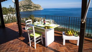 A terrace with a table set for dining, overlooking a coastal view with a mountain in the background.