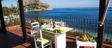 A terrace with a table set for dining, overlooking a coastal view with a mountain in the background.