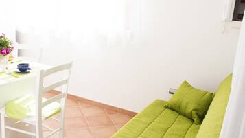 A bright room with a green sofa, white chairs, and a dining table.