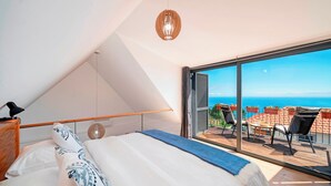 Une chambre dotée d’un grand lit, d’un ventilateur de plafond et offrant une vue sur l’océan grâce à une porte-fenêtre coulissante.