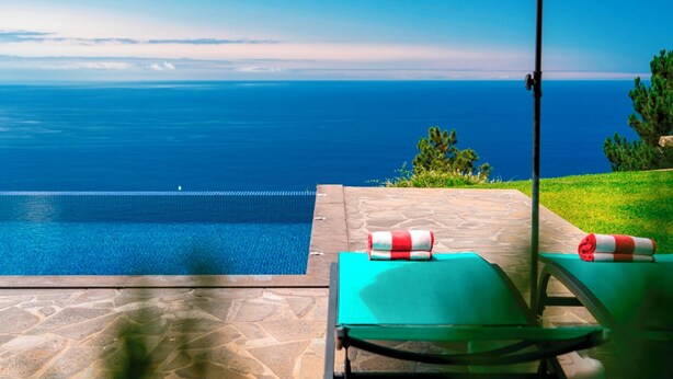 Une piscine avec vue sur l’océan, une chaise longue et un parasol.