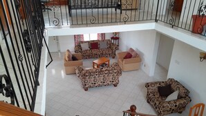A spacious living area with patterned sofas and a wooden coffee table, a balcony with a railing, and a potted plant. - Spacious Air Conditioned 4 bed detached house near Miami Beach (Oistins)