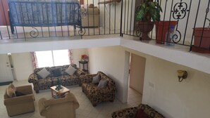 A spacious living area with multiple sofas and a dining table. There is a balcony with potted plants and a railing. - Spacious Air Conditioned 4 bed detached house near Miami Beach (Oistins)