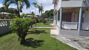 A residential area with a well-maintained lawn, a small tree, and a building with a balcony. - Spacious Air Conditioned 4 bed detached house near Miami Beach (Oistins)