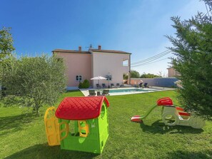 Una casita de juegos verde con techo rojo, una piscina y un columpio en un patio trasero.