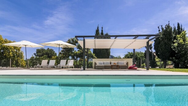 A swimming pool with lounge chairs and umbrellas, a covered seating area, and trees in the background.