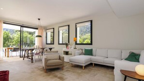 A spacious living room with a large white sectional sofa, a beige armchair, and a dining area with a wooden table and chairs.