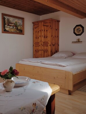 Un dormitorio con cama de madera, una mesita de noche con un florero y un cuadro en la pared, además de un armario de madera.
