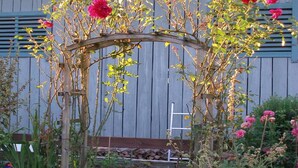 A wooden arbor with pink flowers, a bench, and a stone wall in the background. - Ferienwohnung Kampenwand, 55 qm Obergeschoss, 2 separate Schlafzimmer (Riedering)