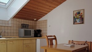 A kitchen with wooden cabinets, a microwave, a coffee maker, and a dining table with chairs. - Ferienwohnung Kampenwand, 55 qm Obergeschoss, 2 separate Schlafzimmer (Riedering)