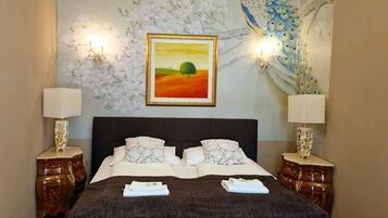 Ein Schlafzimmer mit einem großen Bett, zwei Nachttischen mit Lampen, einem Wandbild von einem Pfau und einem gerahmten Gemälde über dem Bett.