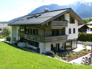 A two-story building with a balcony, a covered outdoor seating area, and a mountain backdrop.