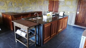 A kitchen with a stone wall, wooden cabinets, a central island with a sink, and pendant lights. - Countryside house with garden and natural pool. (Póvoa de Lanhoso)