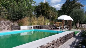 A swimming pool with a wooden deck and a gazebo with a white canopy. - Countryside house with garden and natural pool. (Póvoa de Lanhoso)