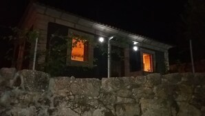 A stone-walled building with two lit windows at night. - Countryside house with garden and natural pool. (Póvoa de Lanhoso)