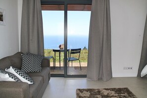 A living room with a sofa, a rug, and a view of the sea through a sliding door.